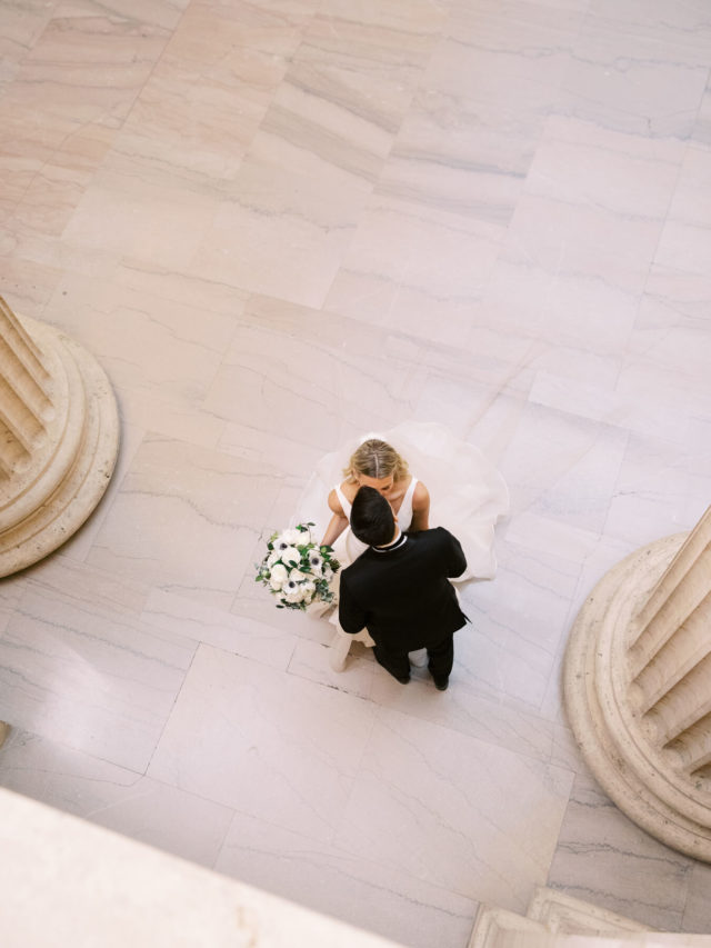 Overhead photo of bride and groom kissing in white elegant ballroom.