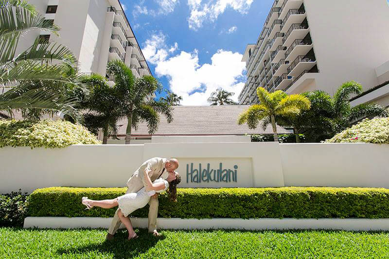 bride and groom kissing in front of Halekulani hotel in Hawaii