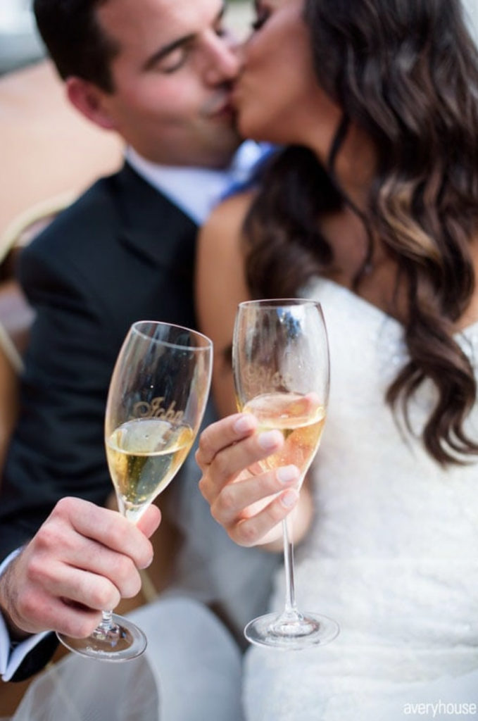 bride and groom kiss while holding champagne glasses