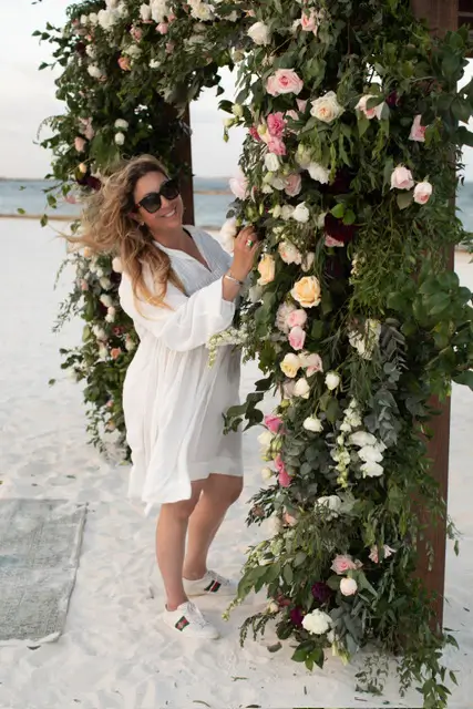 Destination wedding planner, Michelle Durpetti, standing at beachfront wedding floral arch.