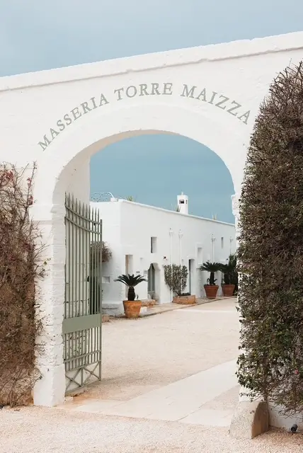 Entrance archway at Masseria Torre Maizza resort in Puglia, Italy, featuring whitewashed architecture and a gated courtyard.