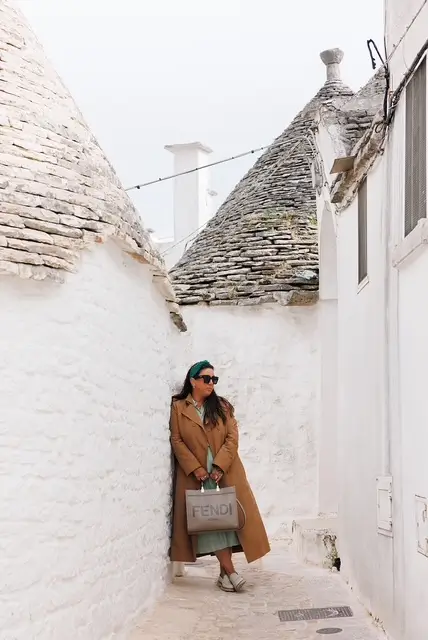 Woman walking through the white stone alleyways and traditional trulli architecture in Alberobello, Puglia, Italy.